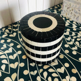 Black and white striped cylindrical container on a patterned surface