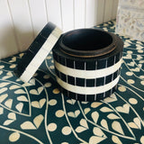 Black and white striped container on a patterned surface