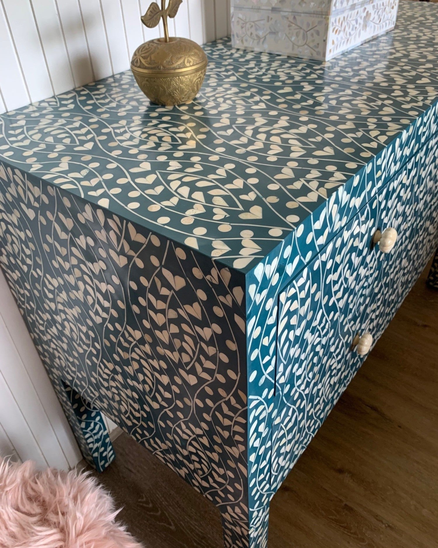 Patterned dresser with decorative items on a wooden floor.