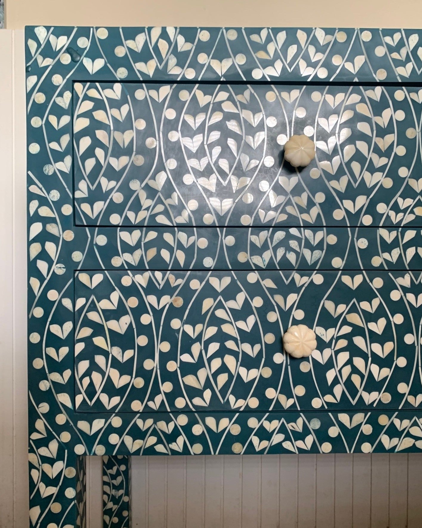 Blue dresser with white floral pattern and white knobs on a light wooden floor.