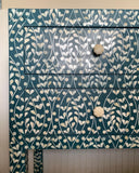 Blue dresser with white floral pattern and white knobs on a light wooden floor.