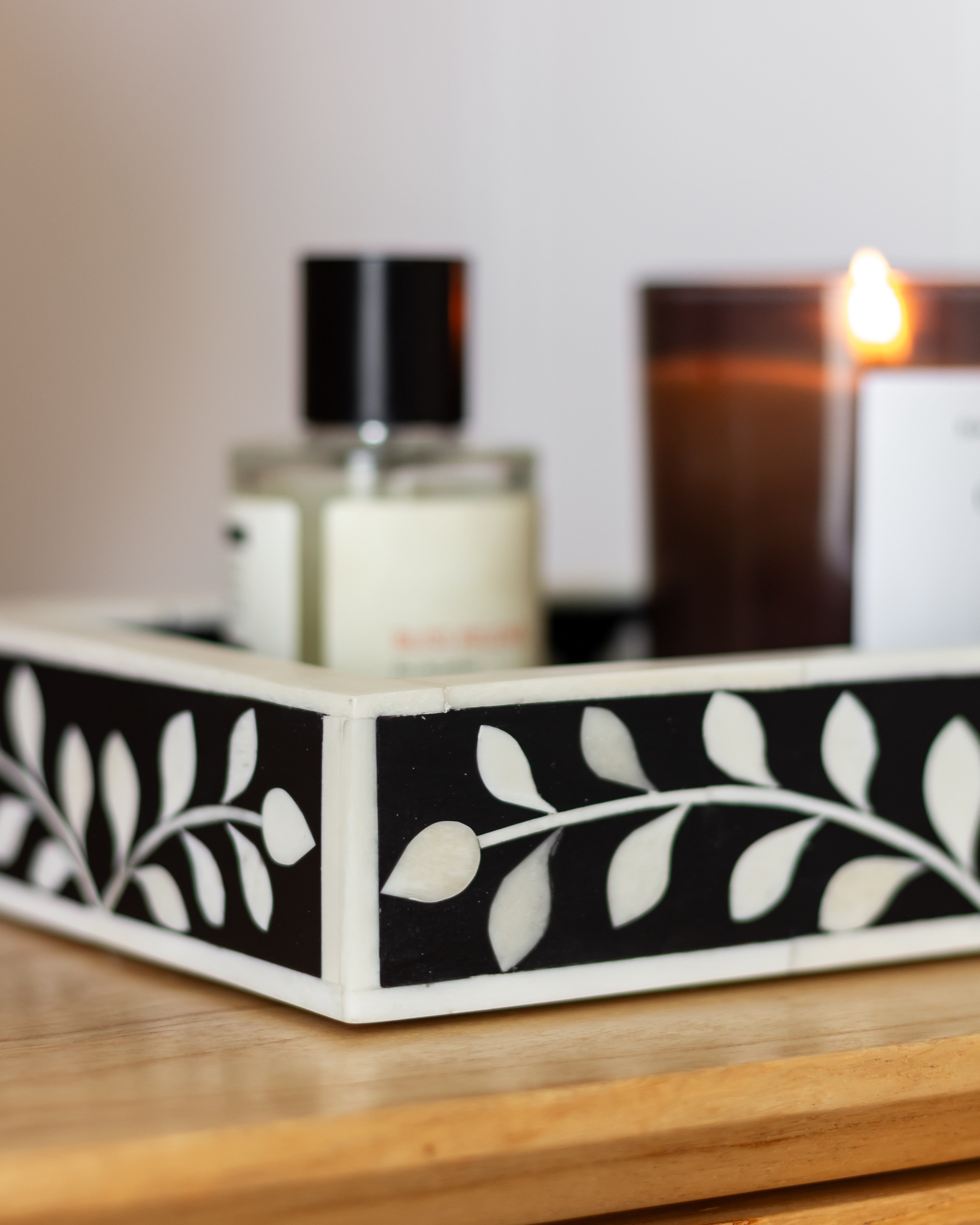 Decorative tray with leaf pattern on a wooden surface next to a bottle and a lit candle.