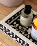 Bottle of perfume and candle on a decorative tray with black and white pattern