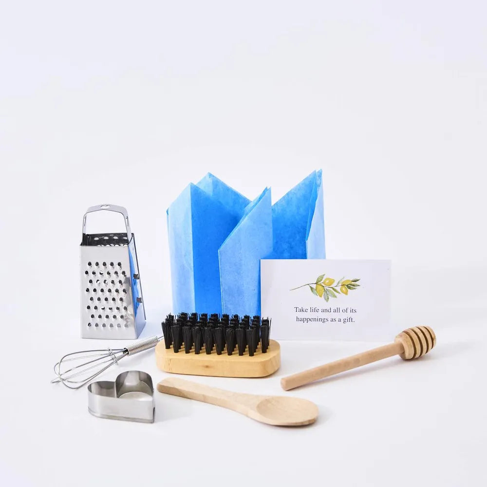 Set of kitchen utensils including a grater, whisk, wooden spoon, and honey dipper on a white background.