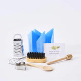 Set of kitchen utensils including a grater, whisk, wooden spoon, and honey dipper on a white background.