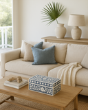 Beige sofa with blue pillows and a decorative box on a wooden coffee table in a living room.