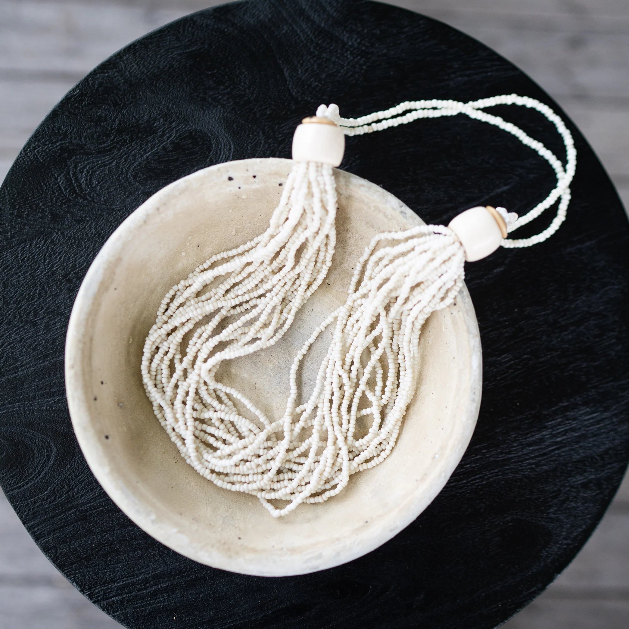 Necklace with white beads in a beige bowl on a dark surface