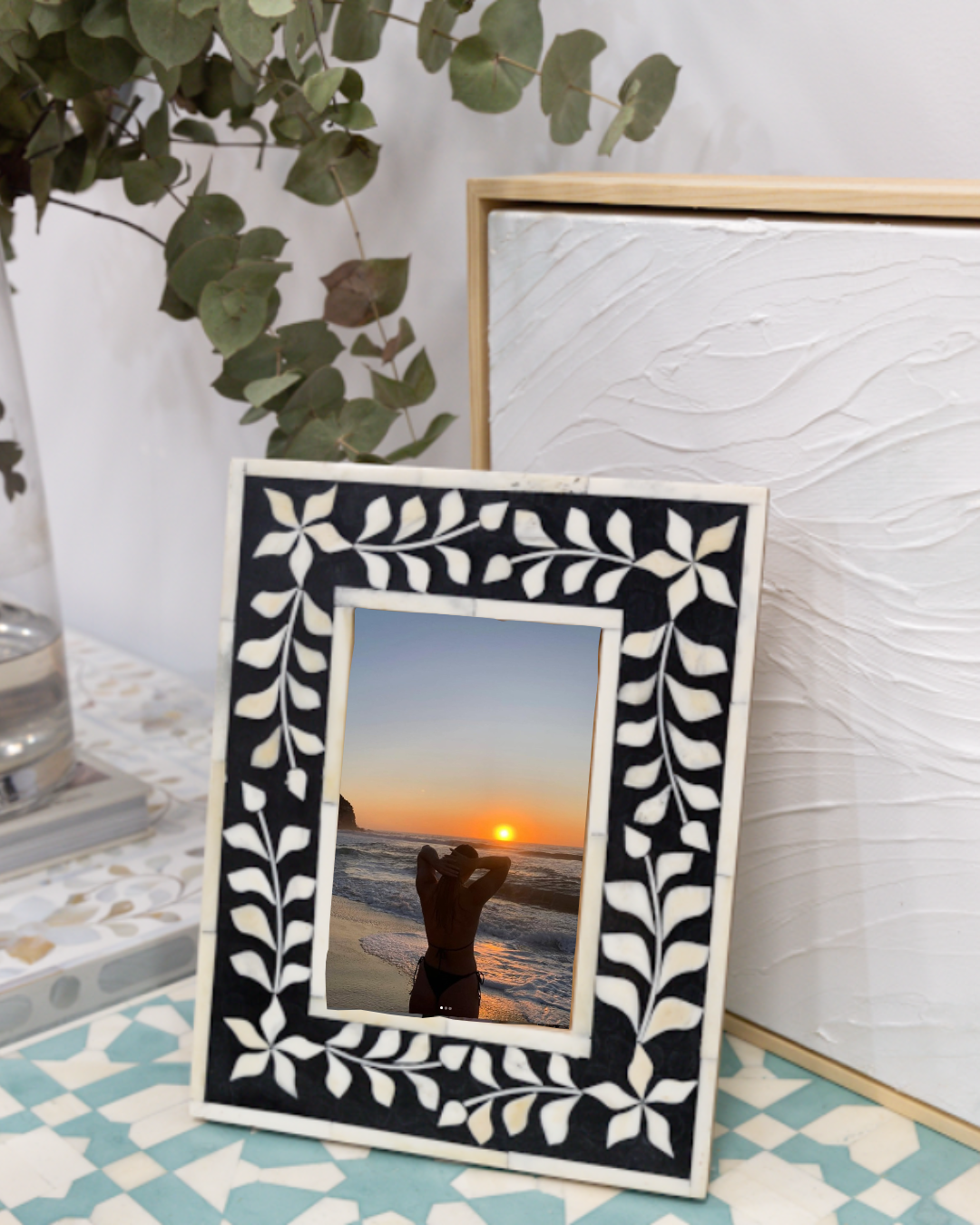 Decorative photo frame with a leaf pattern on a surface with a sunset view.
