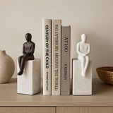 Decorative bookends with statues on a shelf against a beige wall.