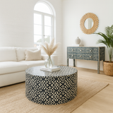 Living room with a patterned ottoman, white sofa, and decorative mirror.