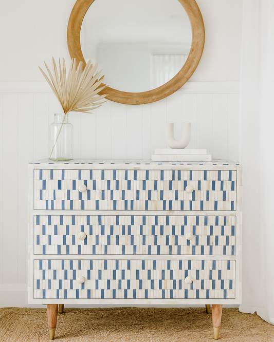 Dresser with blue geometric pattern in a room with a round mirror and decorative elements.