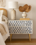 Decorative nightstand with geometric pattern, lamp, and books in a bedroom setting.