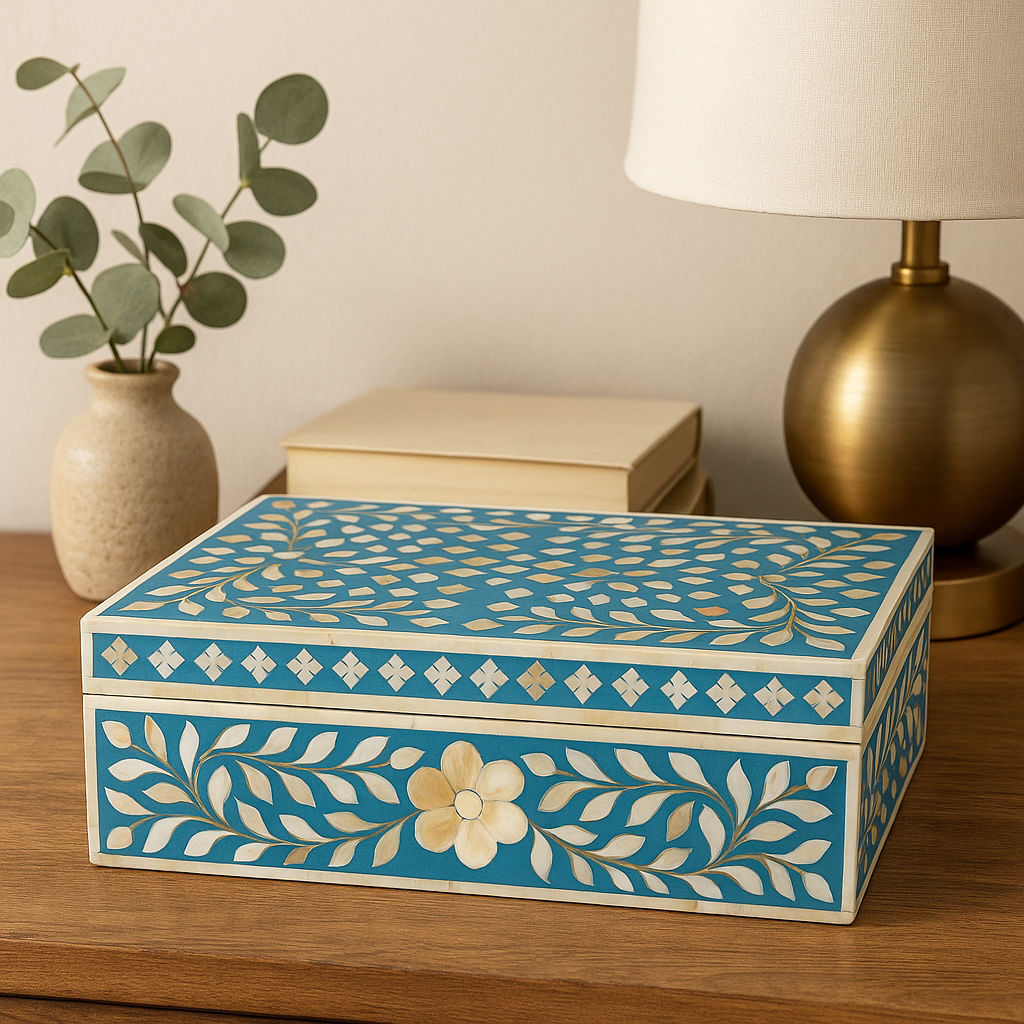 Decorative box with floral patterns on a wooden surface next to a lamp and plant.