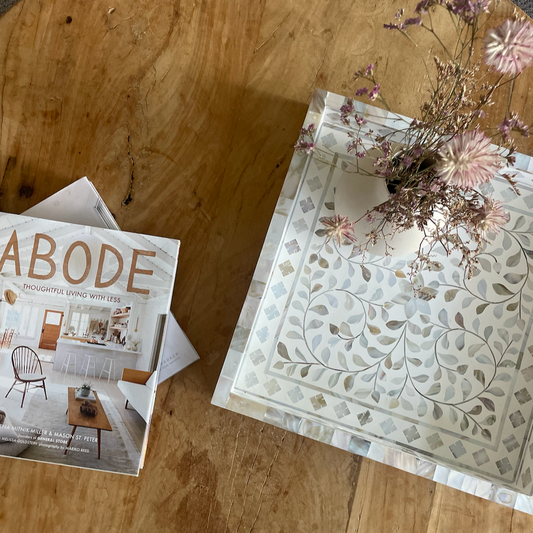 Magazine titled 'ABODE' on a wooden surface with decorative paper and flowers.