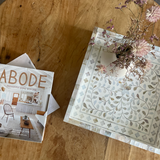 Magazine titled 'ABODE' on a wooden surface with decorative paper and flowers.