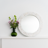 Decorative mirror with floral arrangement on a white surface