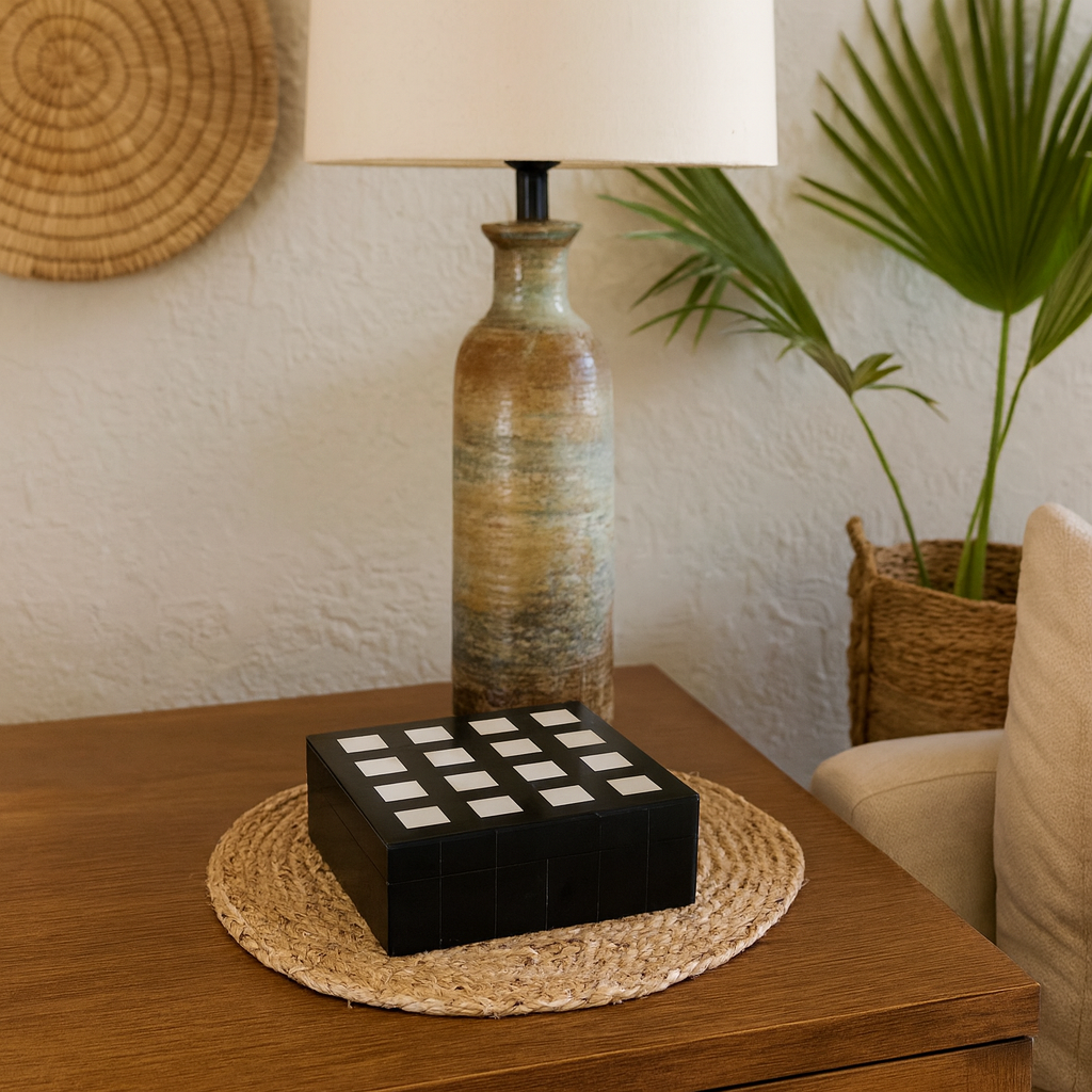 Decorative lamp with a checkered box on a wooden table, surrounded by plants and a woven basket.