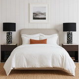 Neatly made bed with white bedding and a brown pillow, flanked by two black lamps on wooden nightstands.