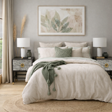 Neatly made bed with beige bedding and green throw, flanked by two nightstands with lamps in a bedroom setting.