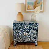 Decorative side table with floral pattern, lamp, and vase in a room setting.