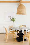 Dining room with a striped table and wooden chairs, featuring a wicker pendant light.