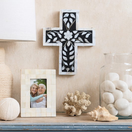Decorative cross with floral design on a shelf with a photo frame and decorative items.