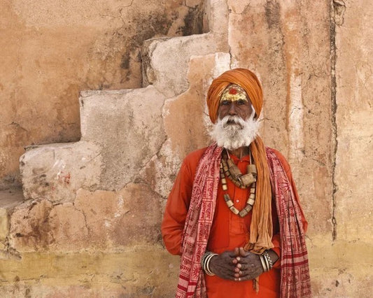 Man in traditional attire standing against a stone wall
