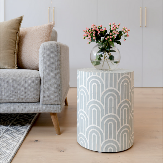 Patterned side table with a vase of flowers next to a gray sofa in a living room.
