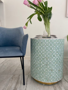 Decorative vase with geometric pattern on a wooden floor next to a blue chair.