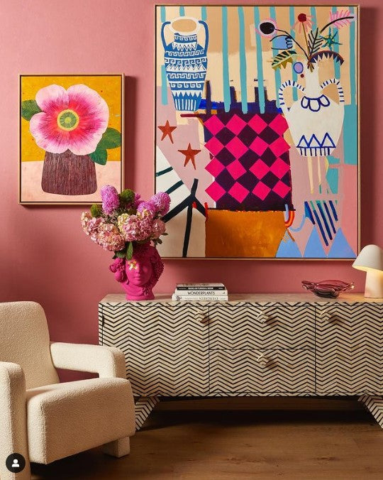 Modern interior with colorful abstract art on a pink wall, a patterned console table, and a floral arrangement.