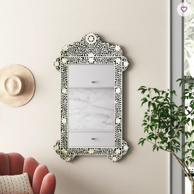 Decorative mirror with intricate design on a wall next to a plant and a hat
