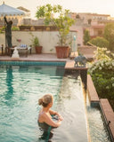 Woman sitting by a pool with a scenic background of buildings and greenery.
