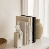 Decorative bookends with a white figurine on top of books on a shelf.