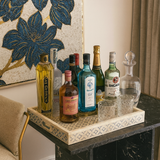 Tray with various bottles and glasses on a table with decorative wall art in the background