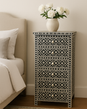 Decorative nightstand with geometric pattern next to a bed with white bedding.