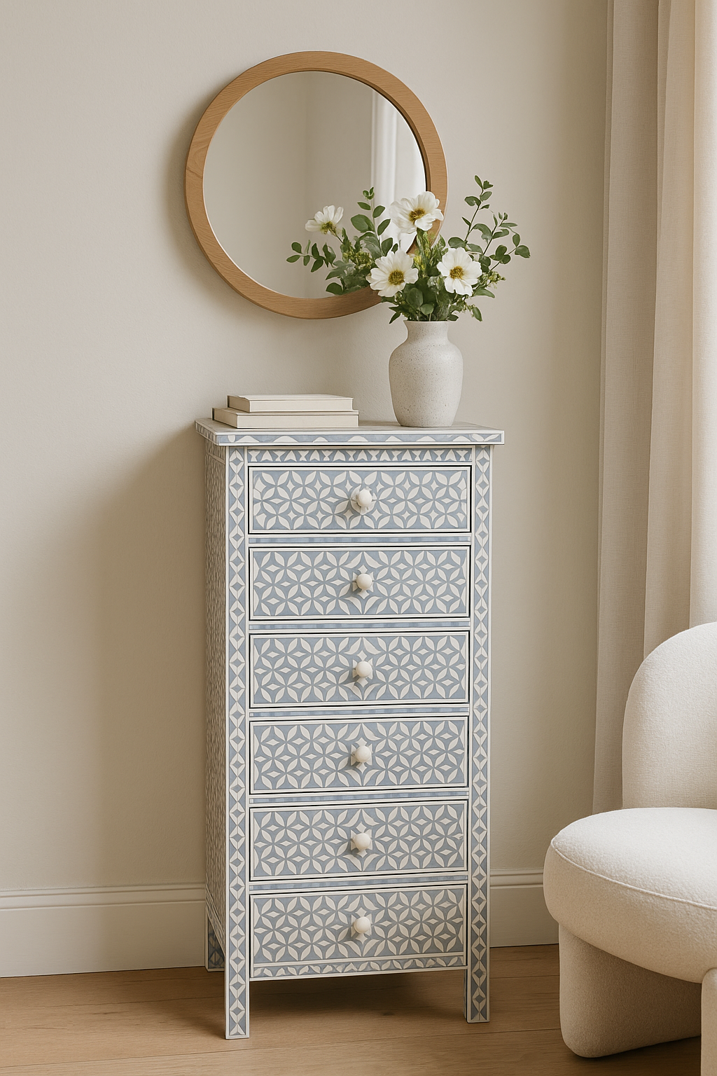 Decorative chest of drawers with a patterned design, round mirror, and vase with flowers on a beige wall.