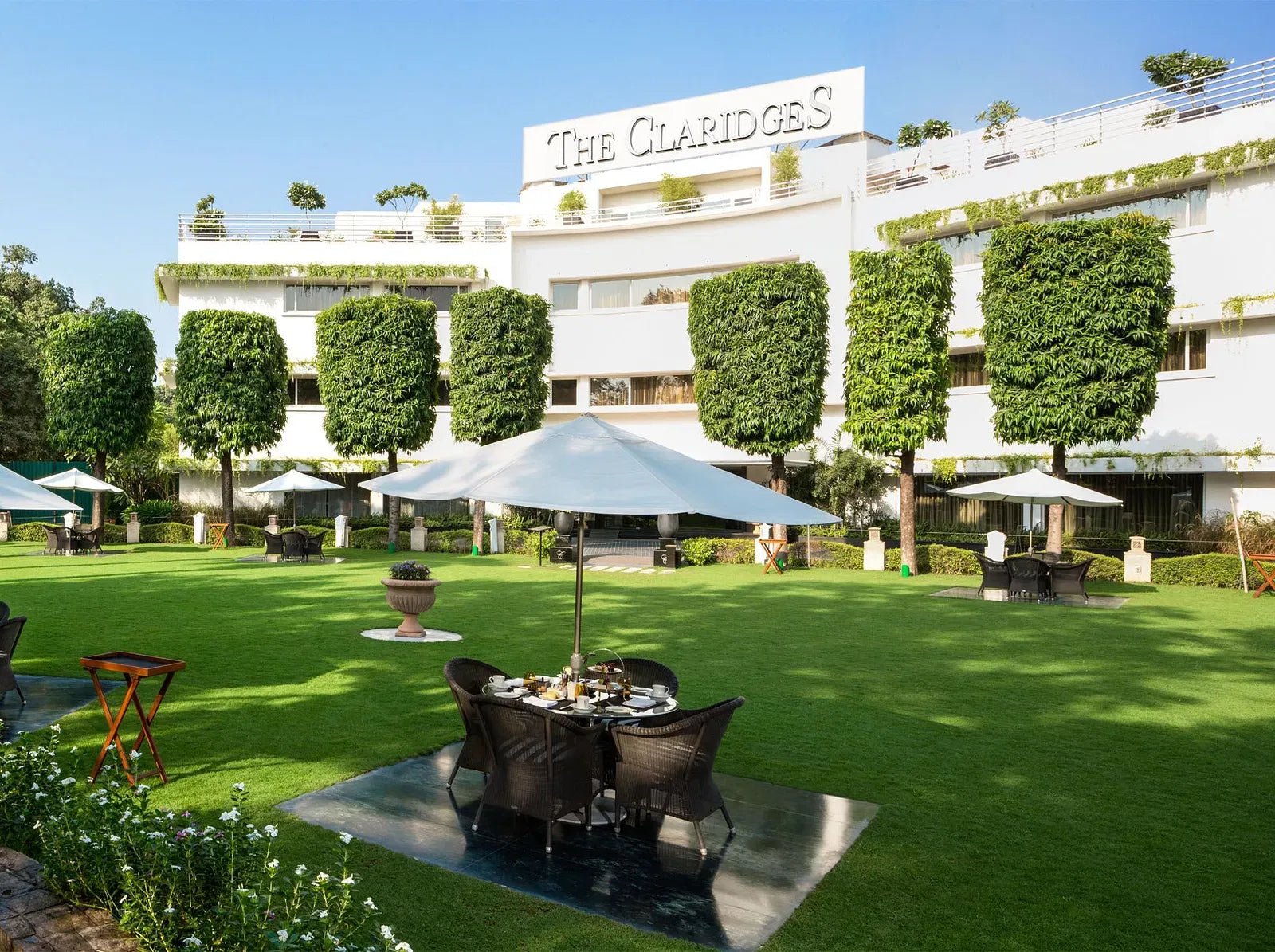 Outdoor seating area with tables and umbrellas in front of The Claridges hotel.