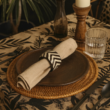 Dining table setting with wooden plates, woven placemat, and patterned tablecloth.