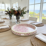 Dining table setting with floral arrangements, a pink patterned tray, and woven placemats.