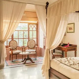 Deluxe room with canopy bed, chairs, and large window.