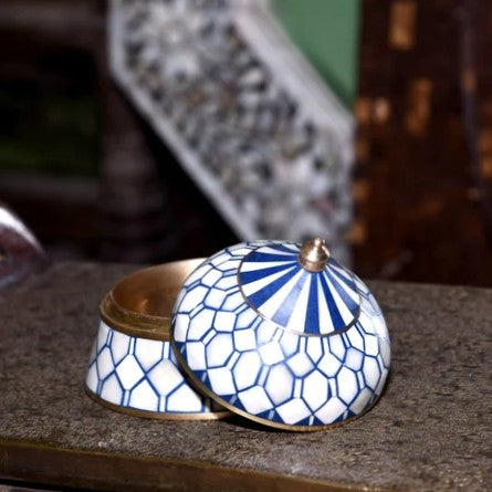 Decorative blue and white mosaic container with gold accents on a textured surface.