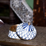 Decorative blue and white mosaic container with gold accents on a textured surface.