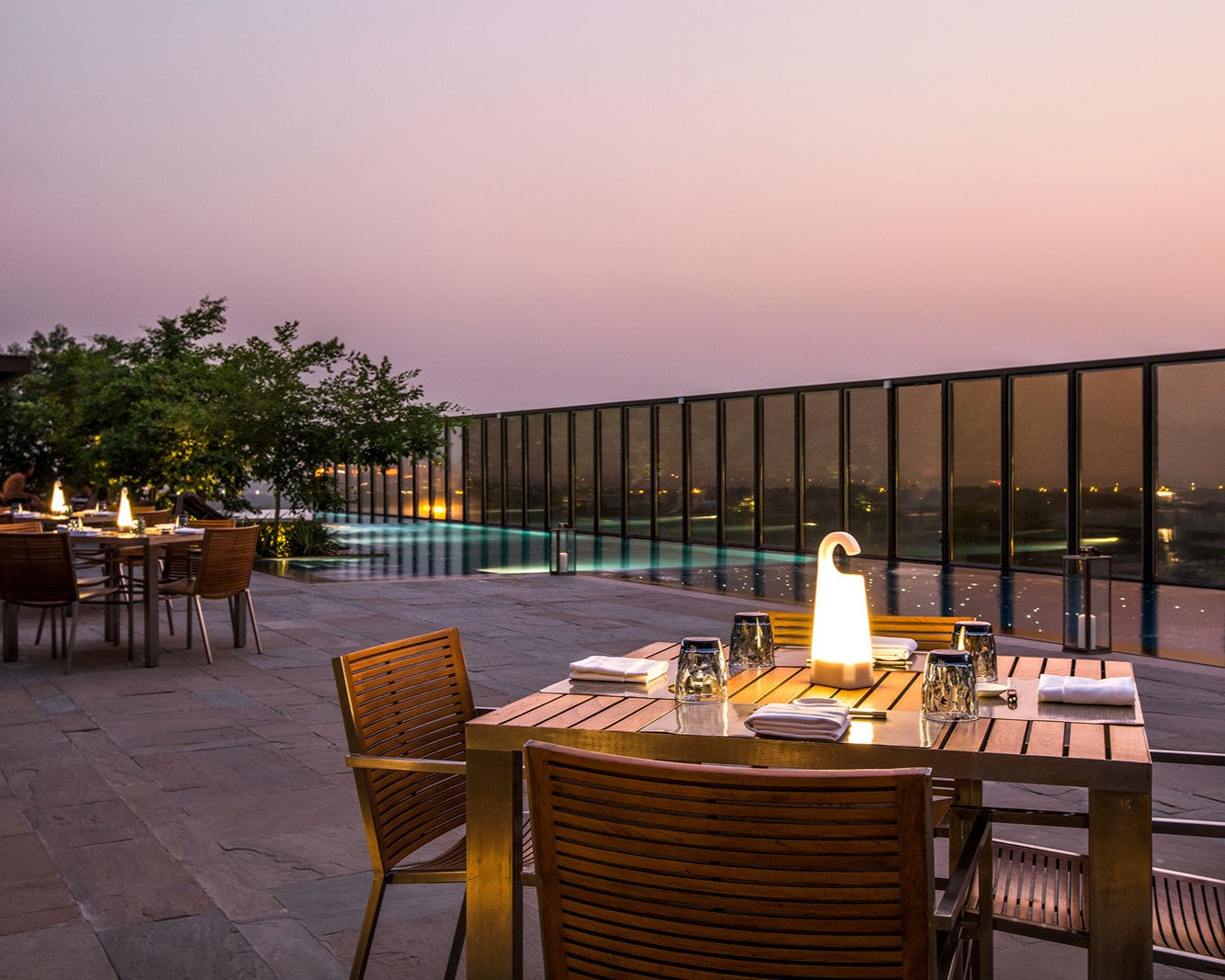 Evening outdoor dining area with wooden tables and chairs by a poolside.