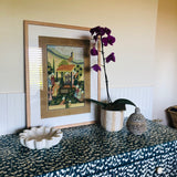 Framed artwork on a table with a purple orchid and decorative items.